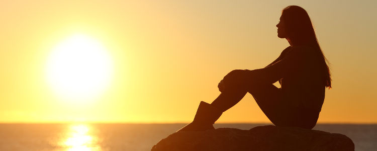 Woman silhouette watching sun in a sunset